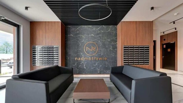 Un lobby moderno con dos sofás, una mesa de centro y una pared de mármol con un logotipo.