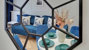 Una habitación con un sofá azul, una mesa blanca con cuencos verde agua y un jarrón con plantas secas.