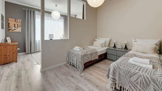 A modern bedroom with two beds, a wooden dresser, a large mirror, and a hanging light fixture. - Gdynia | 800 metres to the beach | City Centre (Gdynia)