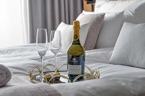 Ein Bett mit einer Weinflasche, zwei Gläsern und einem Tablett mit Pralinen.
