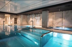 Ein moderner, überdachter Swimmingpool mit klarem Wasser, Glaswänden und einem minimalistischen Design.
