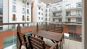 En balkon med et bord og stole, med udsigt over en boligbygning med flere balkoner og vinduer.