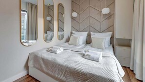 A hotel room with a large bed, three wall mirrors, a headboard with a geometric pattern, and a bedside table. - Waterlane E6 | Spa, Pool & Gym | River View (Gdańsk)
