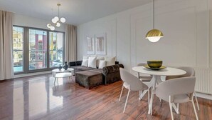 A modern living room with a sofa, ottoman, dining table, chairs, and pendant lighting. - Waterlane E6 | Spa, Pool & Gym | River View (Gdańsk)