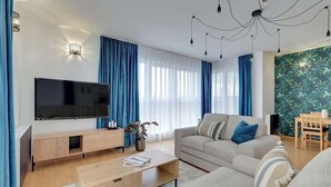 Una sala moderna con televisor de pantalla plana, un sofá, una mesa de centro y un comedor con mesa y sillas.