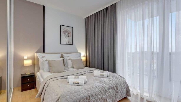 Un dormitorio moderno con una cama grande, una mesita de noche, una obra de arte en la pared y cortinas translúcidas.