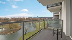 Un balcón con barandilla de vidrio que da a un río y al paisaje urbano.