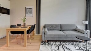 Un soggiorno moderno con un divano grigio, un tavolo da pranzo in legno con sedie, un tappeto bianco e nero e un'opera d'arte incorniciata appesa al muro.