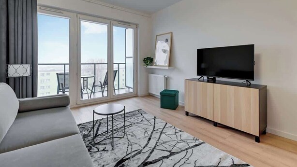 Un soggiorno moderno con divano, televisore su un mobile in legno, un tavolino rotondo e vista panoramica attraverso ampie finestre.