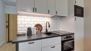 Una cucina moderna con mobili bianchi, un piano di lavoro nero, un lavandino in acciaio inossidabile, un bollitore, una macchina da caffè e un forno a microonde.
