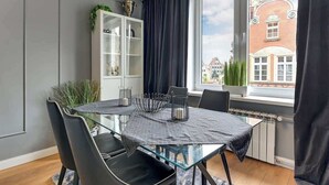 Zona pranzo con tavolo in vetro, sedie nere, un mobile con ante in vetro e vista su un edificio in mattoni rossi attraverso una finestra.