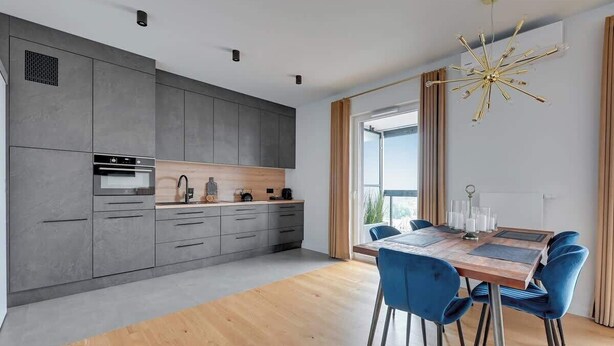 A modern kitchen with grey cabinets, a wooden countertop, and a dining area with a wooden table and blue chairs. - Horizontal Sea & City view | Gdynia | 3 bedrooms (Gdynia)