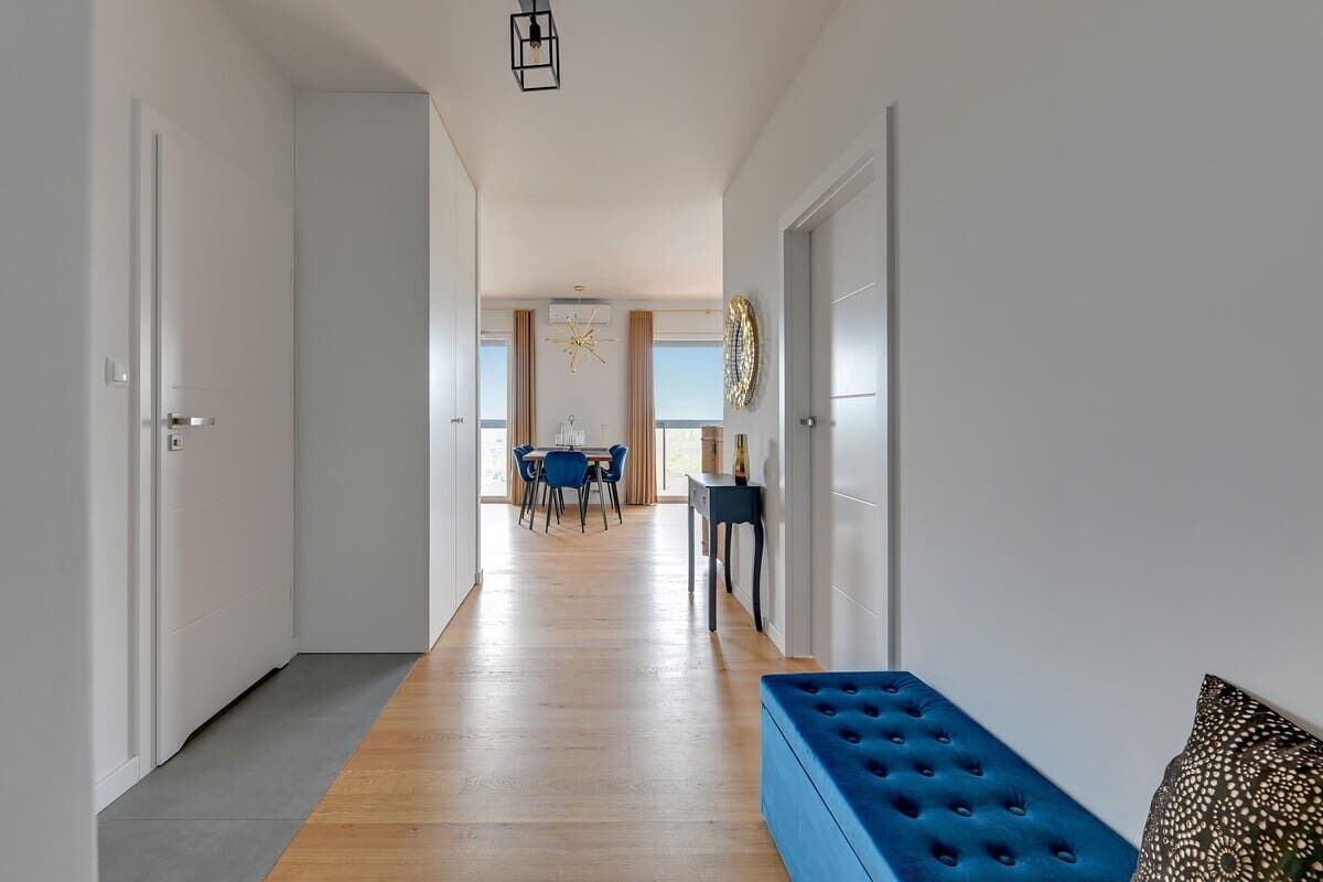 A hallway with a blue bench, a dining area with a table and chairs, and a view through to a room with a large window.