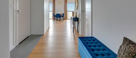 A hallway with a blue bench, a dining area with a table and chairs, and a view through to a room with a large window.