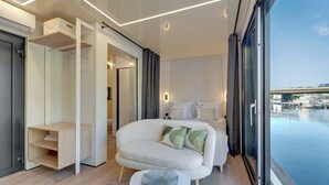 A modern hotel room with a large window, a sofa, a small table, and a built-in wardrobe. - Houseboat Aurora | Old Town | Romantic | Sauna (Gdańsk)