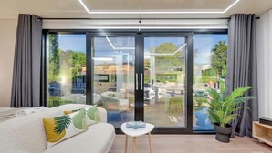 A modern living room with a sofa, a small table, a potted plant, and a sliding glass door leading to an outdoor area. - Houseboat Aurora | Old Town | Romantic | Sauna (Gdańsk)