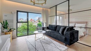 A modern living room with a black sofa, a round coffee table, and a large window offering a city view. - Rezydencja Wintera 1 | River View (Gdańsk)