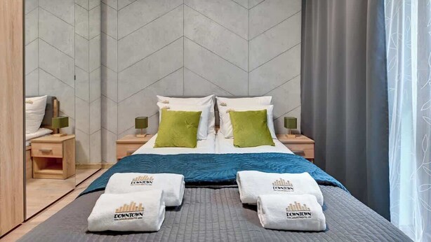 A hotel room with a large bed, two bedside tables, a nightstand, and a view of the city skyline. - Zajezdnia Wrzeszcz 9 | Balkony | Parking (Gdańsk)