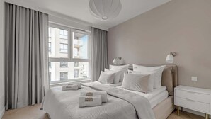 A modern hotel room with a large bed, a bedside table, a lamp, and a view of the city through a window. - Przystań Letnica 20 | Comfortable Stay & Parking (Gdańsk)