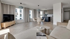 A modern living room with a flat-screen TV, a sofa, a dining table with chairs, and a kitchen area in the background. - Przystań Letnica 20 | Comfortable Stay & Parking (Gdańsk)