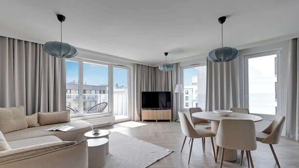 A modern living room with a sofa, dining table, chairs, a TV, and large windows. - Przystań Letnica 20 | Comfortable Stay & Parking (Gdańsk)