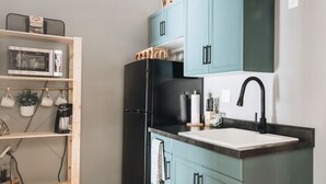 A compact kitchen with teal cabinets, a black refrigerator, a sink, and a 'WELCOME' sign. - The Little Building | Historic Hocking Hills (Logan)