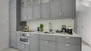 Una cocina moderna con gabinetes grises, horno empotrado, lavamanos y cafetera.