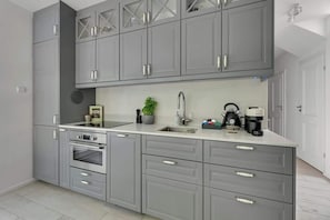A modern kitchen with grey cabinets, a built-in oven, a sink, and a coffee machine.