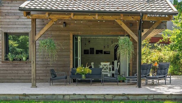 Una casa de madera con un porche cubierto, mobiliario exterior y plantas colgantes.