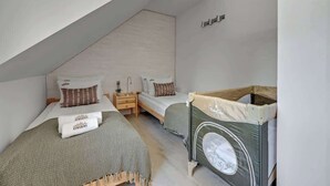 Un dormitorio con dos camas, una cuna de madera y un techo inclinado.