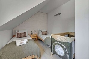 A bedroom with two beds, a wooden crib, and a sloped ceiling.