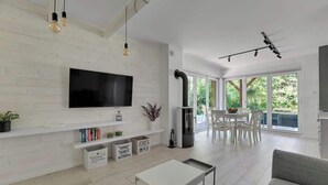 Una sala de estar moderna con televisor de pantalla plana, chimenea, comedor con mesa y sillas, y ventanas amplias.