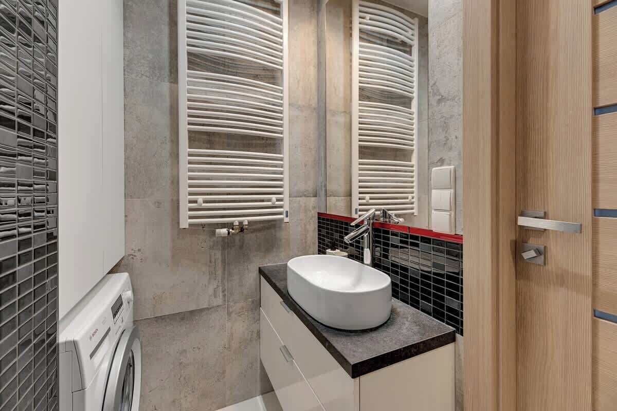 Un baño moderno con lavadora integrada, lavamanos independiente y un espejo con revestimiento blanco y negro.