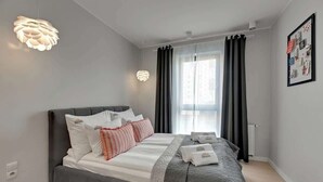 A modern hotel room with a large bed, a bedside table, a window with curtains, and a wall-mounted light fixture. - Browar Gdański | Best Location (Gdańsk)