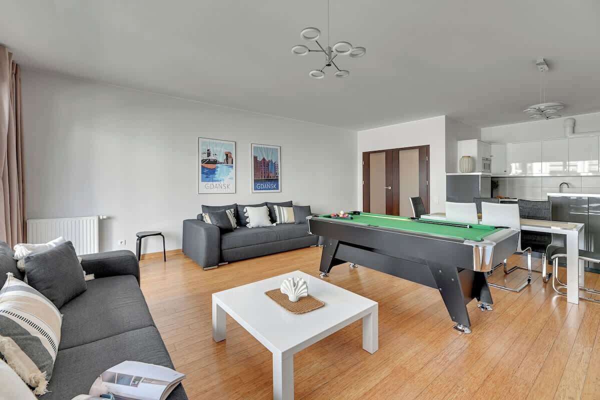 A modern living room with a pool table, grey sofa, and a dining area.