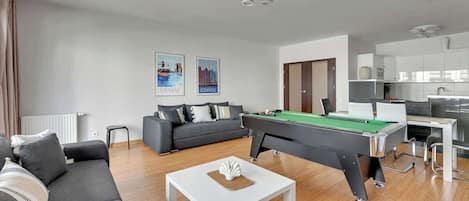 A modern living room with a pool table, grey sofa, and a dining area.