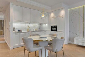 Une cuisine moderne avec des meubles blancs, une table de salle à manger ronde entourée de chaises et un pare-feu en marbre.