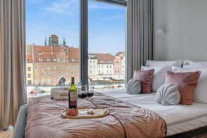 A hotel room with a large window, a bed with a pink bedspread, and a tray with wine and snacks. - DeoPlaza207B | Best view in Gdansk | SPA | Balcony (Gdańsk)