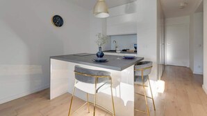 Eine moderne Küche mit Kochinsel, Barhocker, Pendelleuchten und einer sichtbaren Uhr an der Wand.