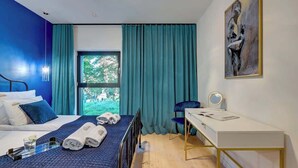 Ein Hotelzimmer mit Bett, Schreibtisch, Stuhl, einem Fenster mit Vorhängen und einem Bild an der Wand.