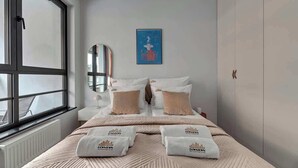 Une chambre d’hôtel avec un lit, une fenêtre, un radiateur, un miroir fixé au mur et un tableau encadré.