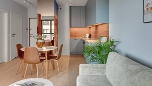 Un salon moderne comprenant un canapé, une table à manger avec des chaises, un coin cuisine et une grande plante.