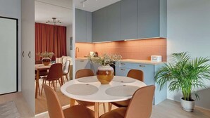 Une cuisine moderne avec des meubles de rangement bleus, un coin repas avec une table ronde et des chaises, et une plante en pot.
