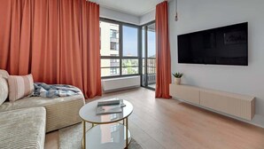 Un salon moderne avec un canapé, une table basse, un téléviseur fixé au mur et de grandes fenêtres dotées de rideaux.