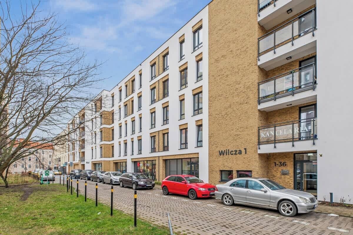 Ein mehrgeschossiges Wohngebäude mit Backsteinfassade, mehreren Balkonen und einem Parkplatz mit Autos.