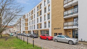 Un edificio residencial de varios pisos con fachada de ladrillo, múltiples balcones y un estacionamiento con automóviles.