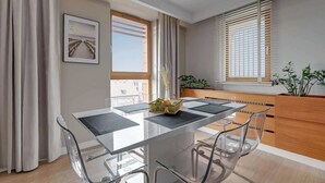 Un espace repas moderne avec une table en verre, des chaises transparentes, des meubles en bois et une vue sur l’extérieur.