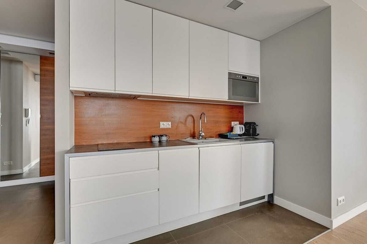 A modern kitchen with white cabinets, a wooden backsplash, and a built-in oven.