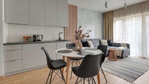 Een moderne keuken met witte kastjes, een eettafel met stoelen, een bank en een vaas met gedroogde bloemen.