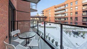 Een balkon met glazen hekwerk, witte stoelen en een tafel.